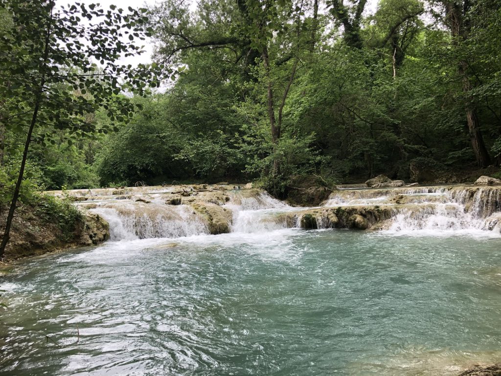 Turquoise river pool below a waterfall, a classic wild swimming in Tuscany spot near Florence
