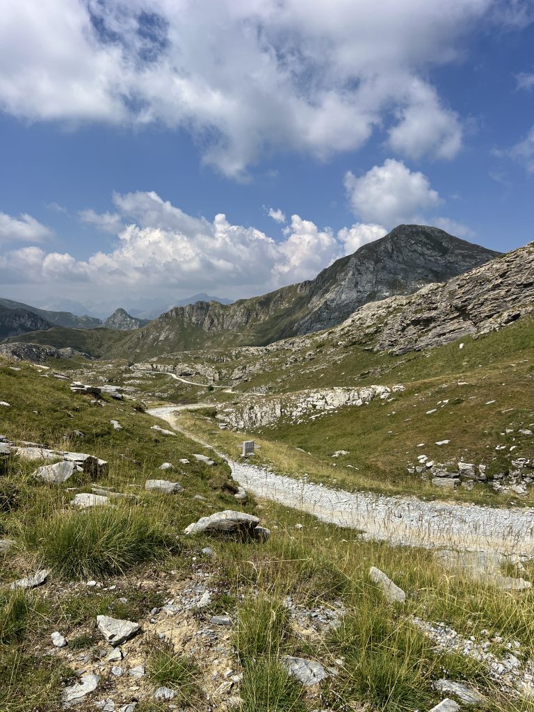 Cyclist riding a gravel bike along the white military road of the Alta Via del Sale, alpine ridge in the background
