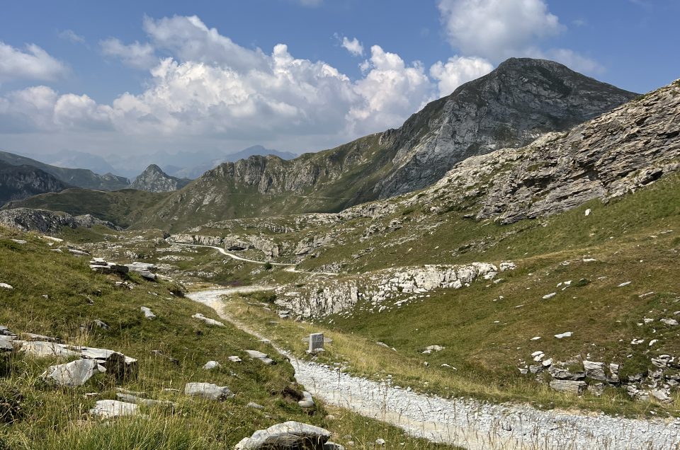 Cyclist riding a gravel bike along the white military road of the Alta Via del Sale, alpine ridge in the background